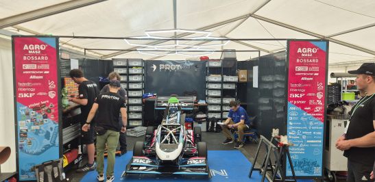 Na zdjęciu bolid i stojący obok niego oraz ścianki reklamowe