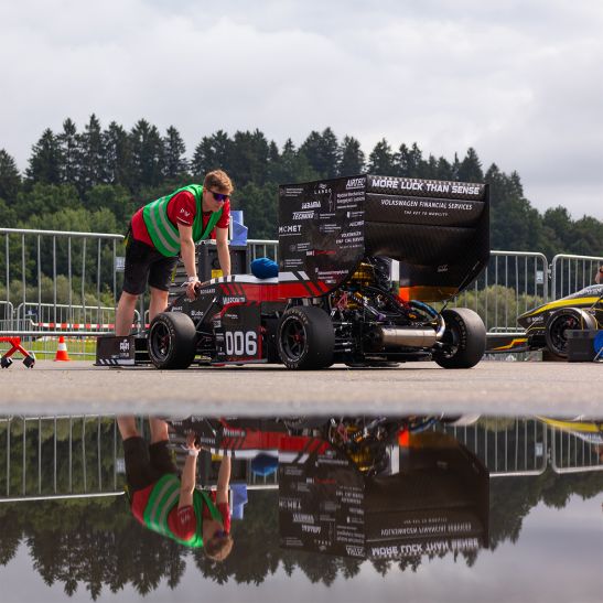 Na zdjęciu bolid i student opierający się o niego rękami 