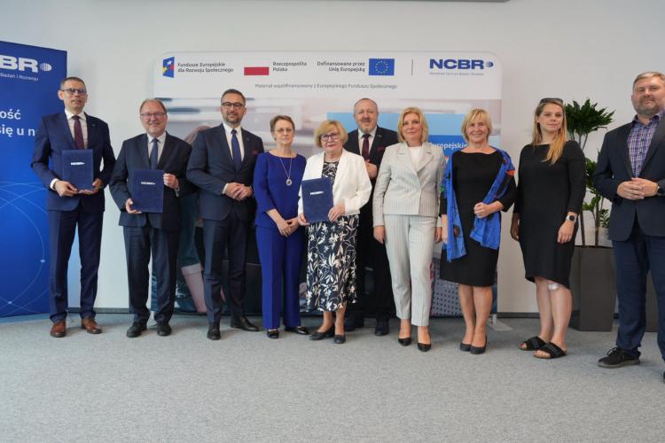 Na zdjęciu grupa stojących osób: przedstawiciele Politechniki Warszawskiej, Sopockiej Akademii Nauk Stosowanych, Zachodniopomorskiego Uniwersytetu Technologicznego w Szczecinie wraz z Ministrem Nauki Marcinem Kulaskiem i Dyrektorem NCBR prof. Jerzym Małachowskim 