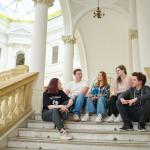 Na zdjęciu pięć osób: trzy kobiety i dwóch mężczyzn siedzi na schodach w Gmachu Głównym Politechniki Warszawskiej